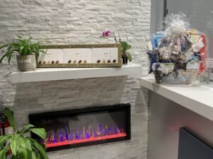 Reception area at Avatar Dental featuring a modern electric fireplace, decorative plants, a gift basket, and a “Welcome” sign